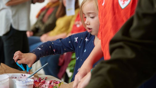 A close-up image of a young child participating in craft activity within people in the foreground and background.